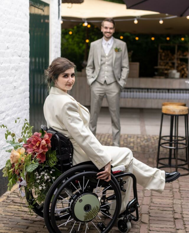 Birgit was op zoek naar inspiratie voor een versierde rolstoel. Helaas kon ze op het internet niets leuks kon vinden... Totdat haar moeder met het winnende idee kwam; bloemen! Daarvoor schakelde ze de hulp van lievelingsleverancier @blouming_floral_art in, met een prachtige rolstoel tot resultaat!⁠
⁠
Lees via de 🔗 in onze bio de tips van Birgit en Jense voor het trouwen in een versierde rolstoel!⁠
⁠
De leveranciers:⁠
Fotograaf: @foto_workshopnl⁠
Locatie: @dewillemshoeve ⁠
Bloemist: @blouming_floral_art⁠
Birgit en Jense: @kreupelino & @jense.es⁠
⁠
#girlsofhonour #trouwen #bruiloft #WijGaanTrouwen #wedding #WeddingInspiration #BruiloftInspiratie #BruiloftBlogger #TrouwenIn2022 #trouwblog #trouwplannen #huwelijk #WijZijnVerloofd #ISaidYes #BrideToBe2022 #WeddingHacks #DutchModernBrides #ModerneBruid #ModernBride #TrouwenInEenRolstoel #WeddingDetails⁠
⁠
ID: Bruid zit in een met bloemen versierde rolstoel en kijkt glimlachend in de camera. De bruid is gekleed in een wit trouwpak met zwarte trouwschoenen. Bruidegom staat op de achtergrond met beide handen in zijn zakken en kijkt lachend in de camera. De bruidegom draagt een grijs driedelig pak met een witte overhemd.⁠